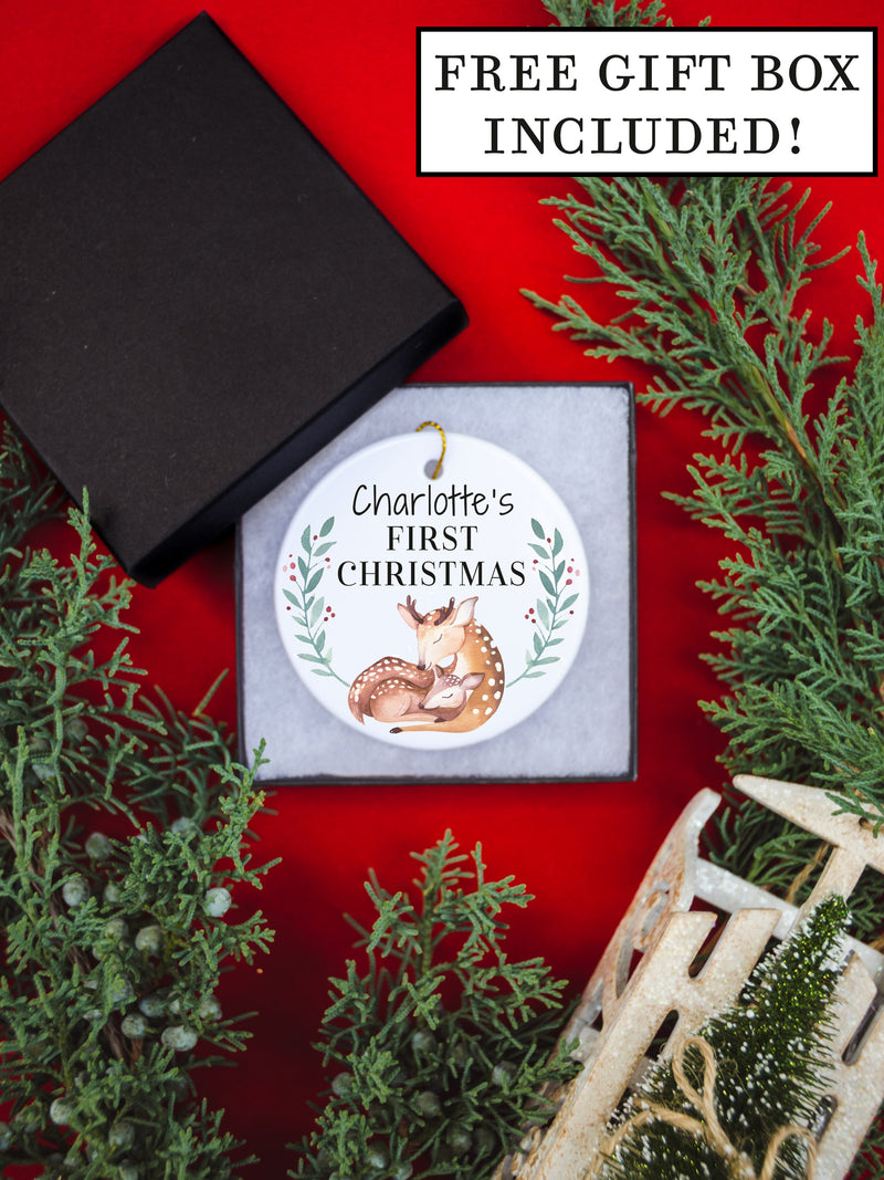 White circular ceramic ornament with the words (Name) First Christmas in the top center and the year. There is a mother dear snuggling her baby doe under the babies name.  Black cursive font.  Ships with gold threaded ornament tie.